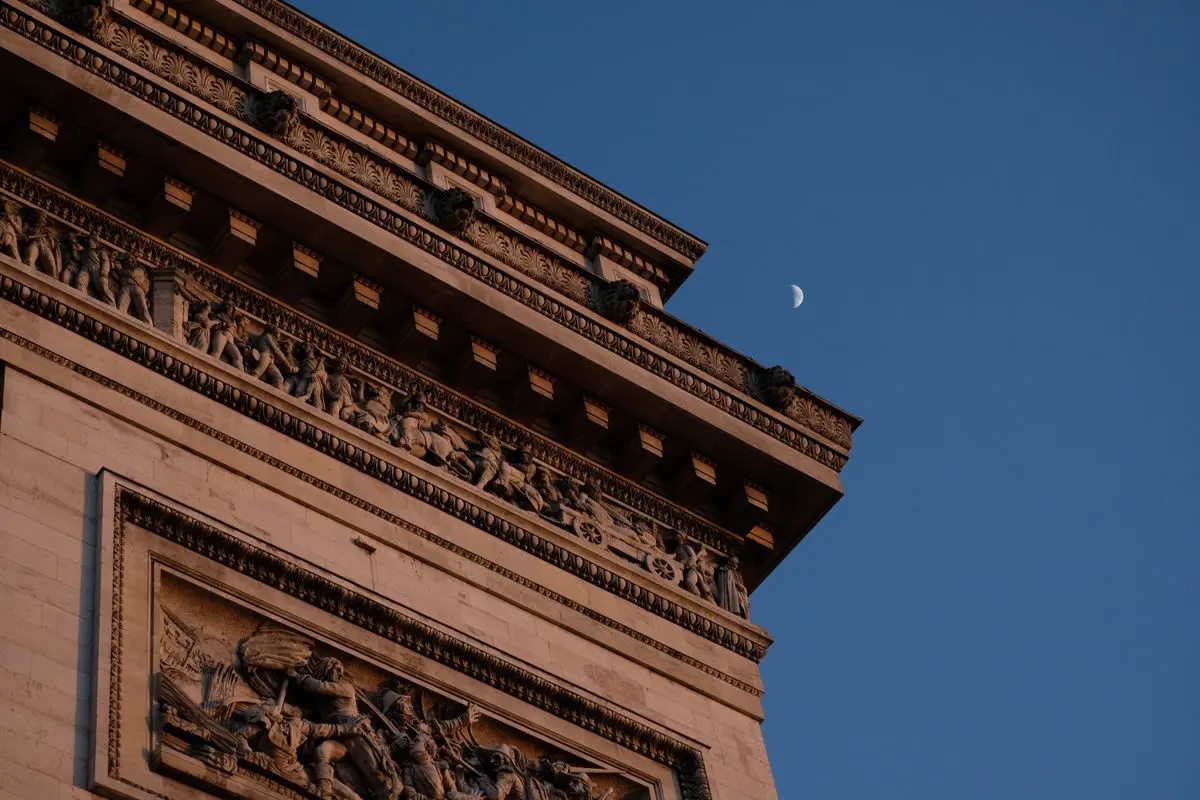 Détail de la corniche sculptée de l'Arc de Triomphe sous un ciel étoilé avec le croissant de lune